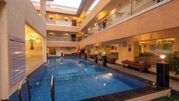 A multi-level indoor swimming pool with clear water, surrounded by lounge areas and a glass balustrade.