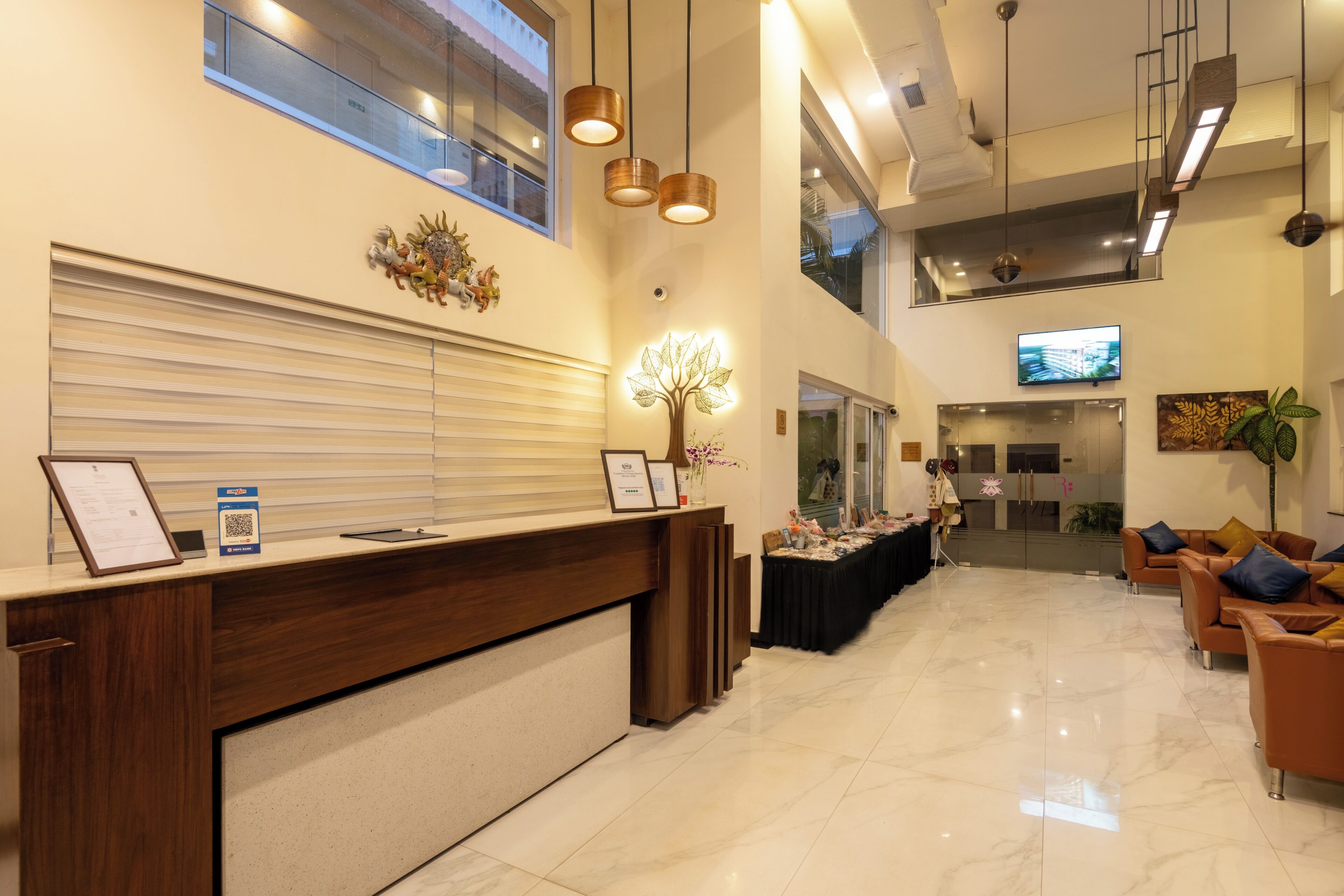 A hotel reception area with a wooden reception desk, a large window, and a flat-screen TV mounted on the wall.