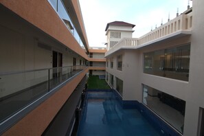 A multi-level indoor swimming pool with glass railings and a small grassy area in the center. - Regenta Central North Goa (Arpora)