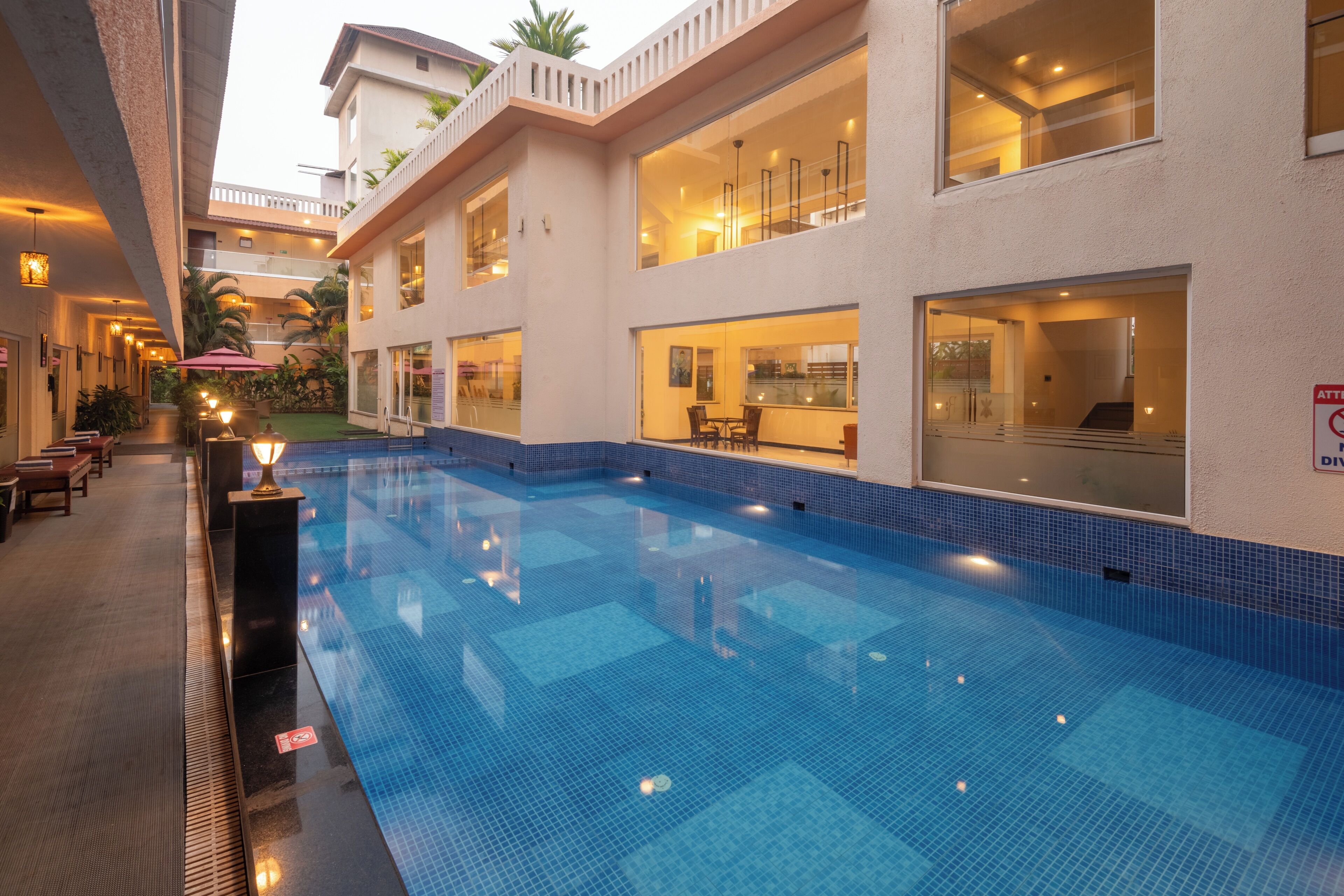 Ein Pool mit einer gefliesten Kante, umgeben von einem Gebäude mit mehreren Fenstern und einem Balkon.