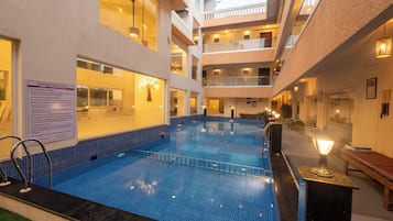 Una piscina interior con suelo de baldosas, rodeada de balcones y un cartel con las normas de la piscina.