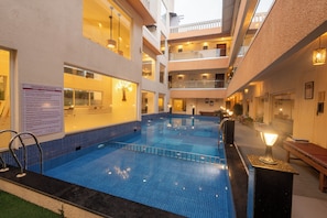Una piscina interior con suelo de baldosas, rodeada de balcones y un cartel con las normas de la piscina.