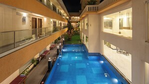 A hotel pool area with a clear view of the pool, lounge chairs, and a small garden. - Regenta Central North Goa (Arpora)