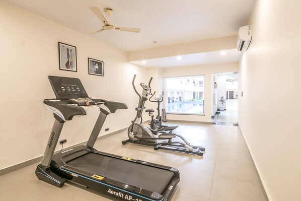 Un gimnasio con cintas de correr, bicicletas estáticas y un ventilador de techo.