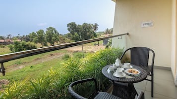 A balcony with a table set for tea, overlooking a rural landscape with trees and fields.