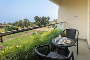 Un balcón con una mesa dispuesta para tomar té, con vistas a un paisaje rural con árboles y campos.