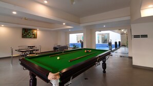 Ein Billardtisch mit grüner Spielbahn, ein weißer Deckenventilator und ein Gemälde an der Wand.