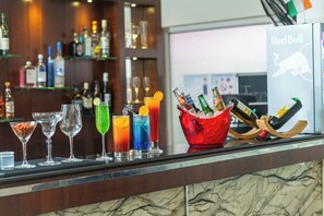 A bar area with a variety of drinks and bottles, a Red Bull logo, and a wooden bar counter. - Regenta Central North Goa (Arpora)