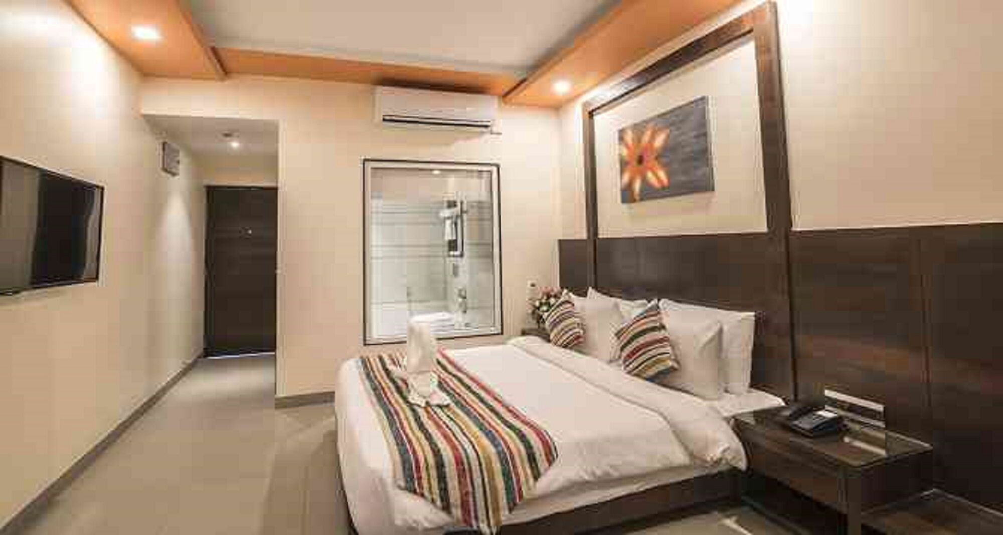A hotel room with a bed, bedside table, and a TV on the wall.