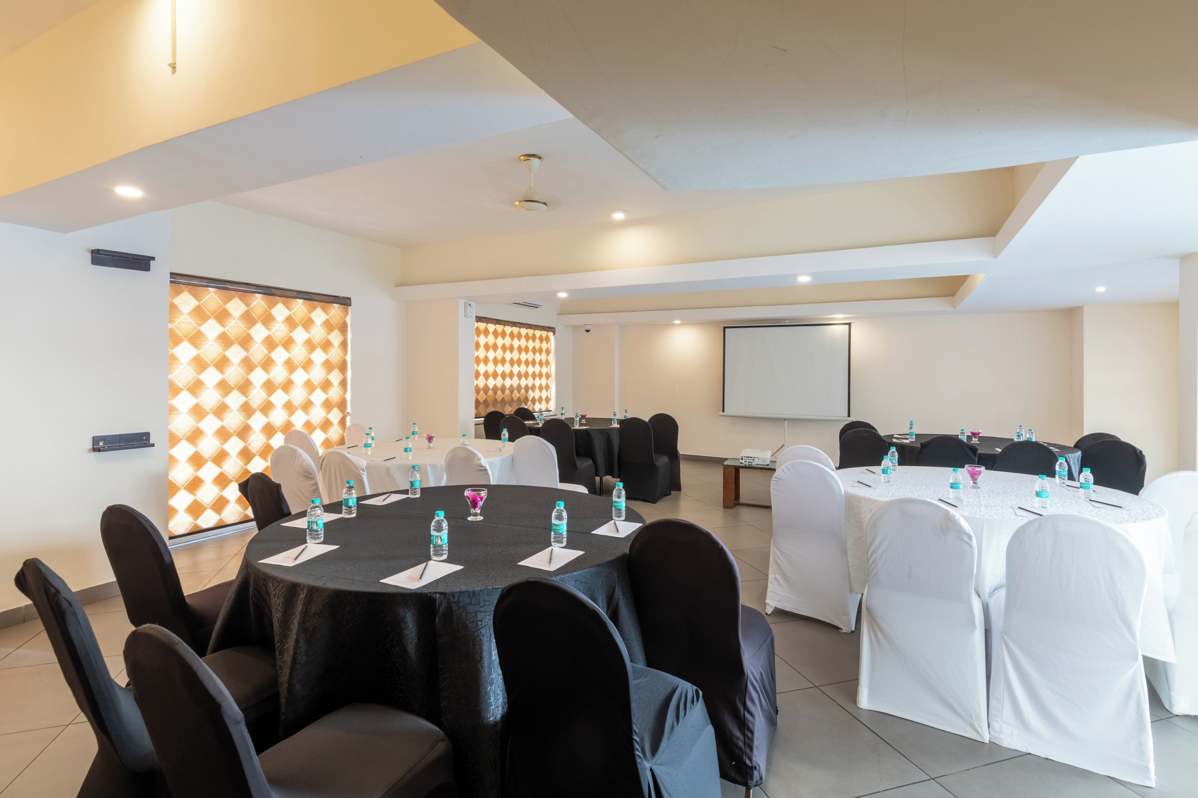 A conference room with round tables, chairs, and a projector screen.