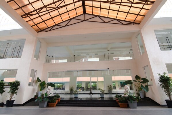 A modern building with a glass facade, a central staircase, and potted plants. - Regenta Central North Goa (Arpora)