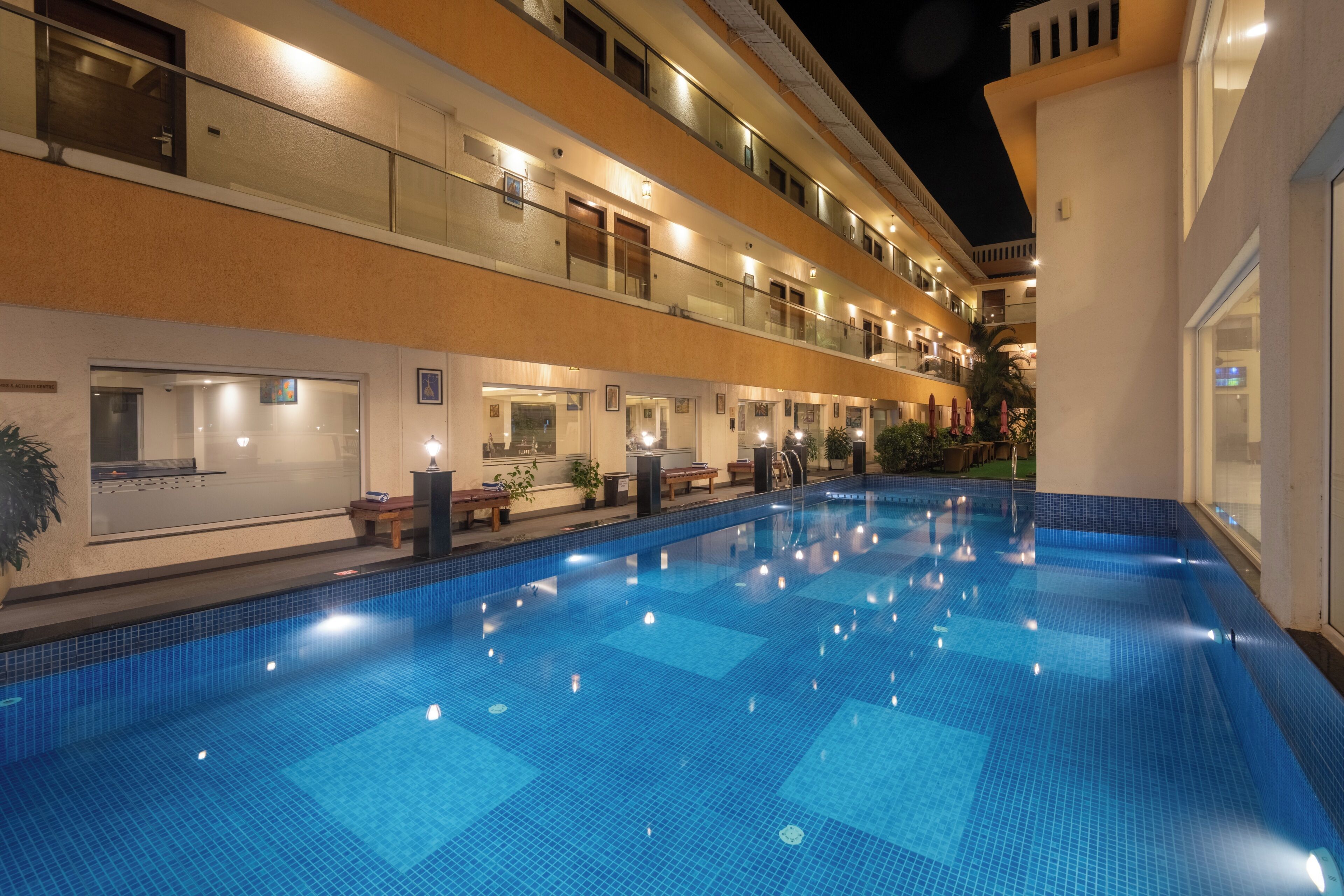 Zona de piscina de hotel con piscina azul cristalina, varios balcones e interior bien iluminado.