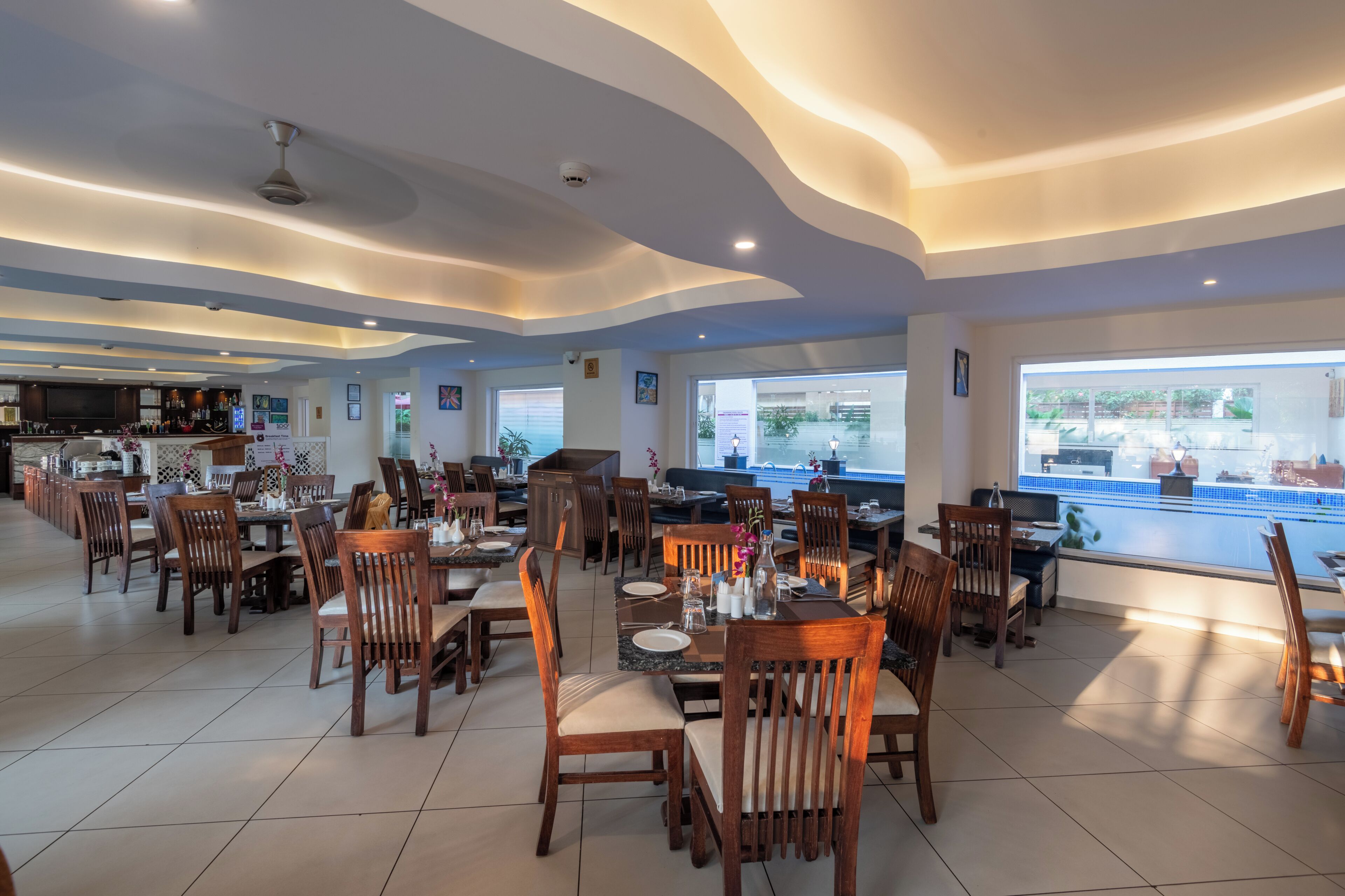 Ein geräumiges Restaurant mit hohen Decken, mehreren Essbereichen und großen Fenstern, die einen Blick ins Freie ermöglichen.