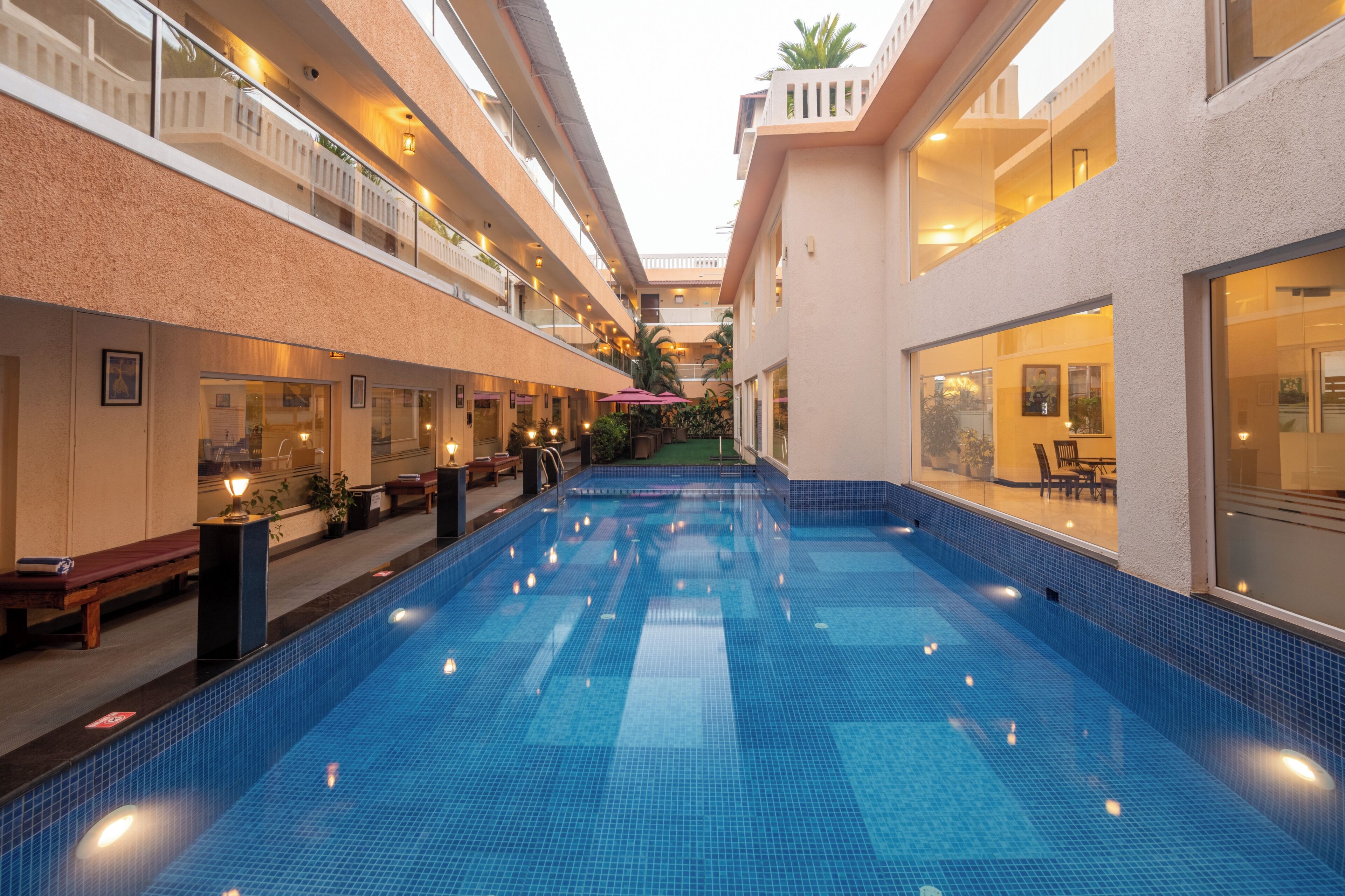 A hotel interior with a central swimming pool, multiple balconies, and indoor seating areas.