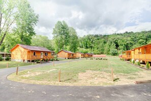 Une rangée de cabanes en bois, séparées par un chemin pavé, et entourées d’une zone herbeuse et d’arbres.