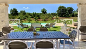 Une terrasse extérieure avec une table et des chaises, une piscine et une vue sur un jardin aménagé.