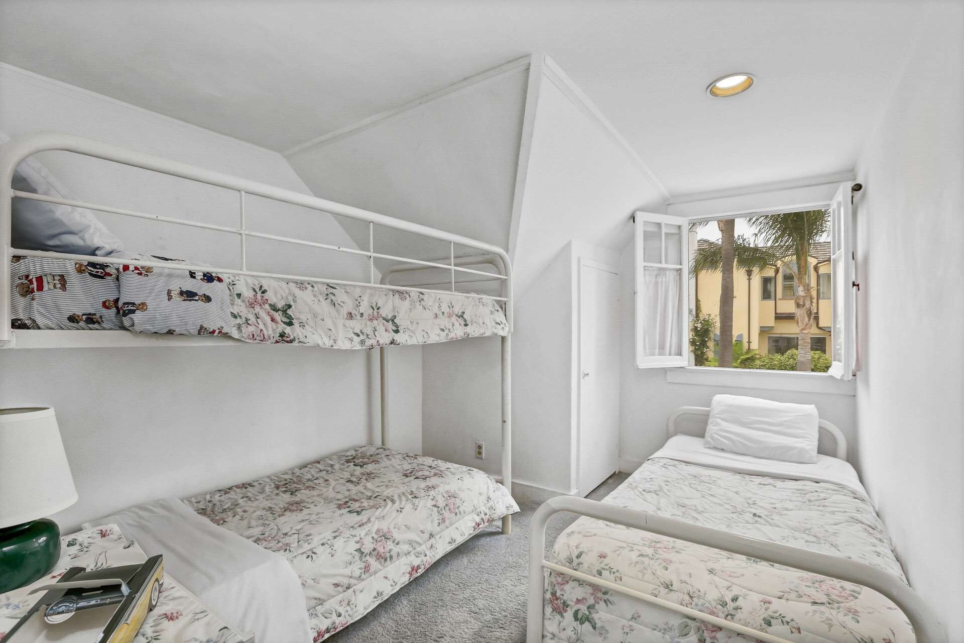 A dormitory room with bunk beds, a window with a view of buildings, and a lamp on the left side.