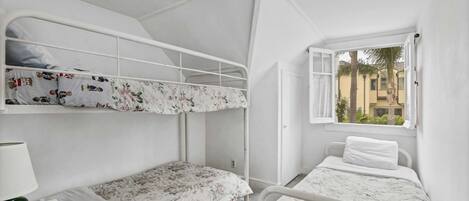 A dormitory room with bunk beds, a window with a view of buildings, and a lamp on the left side.