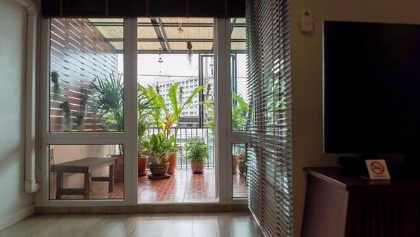 A room with a sliding glass door leading to a balcony with potted plants and a wooden bench. - Private house in city center near Sukhumvit-Rama4 (Khwaeng Khlong Toei)