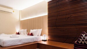 A modern hotel room with a wooden headboard, a bed with white linens, a bedside table with a decorative lamp, and a wooden bench with a geometric cushion. - Private house in city center near Sukhumvit-Rama4 (Khwaeng Khlong Toei)
