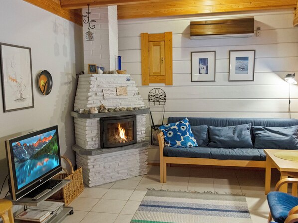 Een gezellige woonkamer met een open haard, een bank, een televisie en een houten plafond.