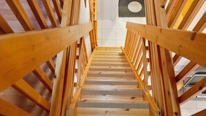 Eine Holztreppe mit Handlauf, die zu einem Raum mit weißer Decke und einem Rundfenster führt.