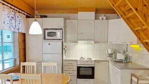 Eine kompakte Küche mit weißen Schränken, einer Mikrowelle, einem Kühlschrank, einem Herd und einem Spülbecken. Es ist ein Esstisch mit Stühlen und ein Fenster mit Jalousien vorhanden.