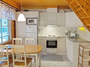 Een compacte keuken met witte kastjes, een magnetron, een fornuis en een spoelbak. Er is een eettafel met stoelen.