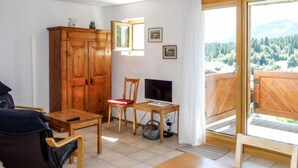 A room with a wooden table, two chairs, a TV, and a view of a forest through a large window. - Girun Eder by Interhome (Flims)