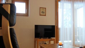 A living room with a TV, a wooden table, a chair, and a window with curtains. - Girun Eder by Interhome (Flims)