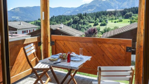 A wooden balcony with a table set for two, overlooking a mountainous landscape with a clear sky. - Girun Eder by Interhome (Flims)