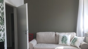 A beige sofa with two green leaf pillows, a white door, and a red chair in a room with a grey wall. - Guest apartment on Petersberg with balcony (Erfurt)
