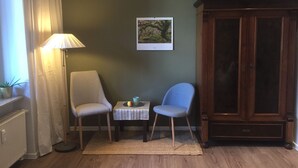 A room with a wooden cabinet, two chairs, a small table with a lamp, and a framed picture on the wall. - Guest apartment on Petersberg with balcony (Erfurt)