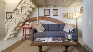 A living room with a sofa, a coffee table with an open book, a wine bottle, and glasses. There is a staircase with a railing and a wall with framed pictures. - An apartment in the heart of Santo Spirito by Mmega (Firenze)