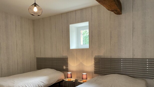 Habitación con dos camas, paredes de paneles de madera, un ventanal pequeño y una lámpara colgante.