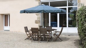 Un patio al aire libre con una mesa y sillas, una sombrilla azul y un edificio con ventana y pared de piedra al fondo.