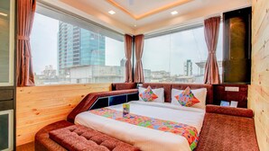 Una habitación de hotel moderna con una cama grande, un banco de madera y vistas a la ciudad a través de amplias ventanas.