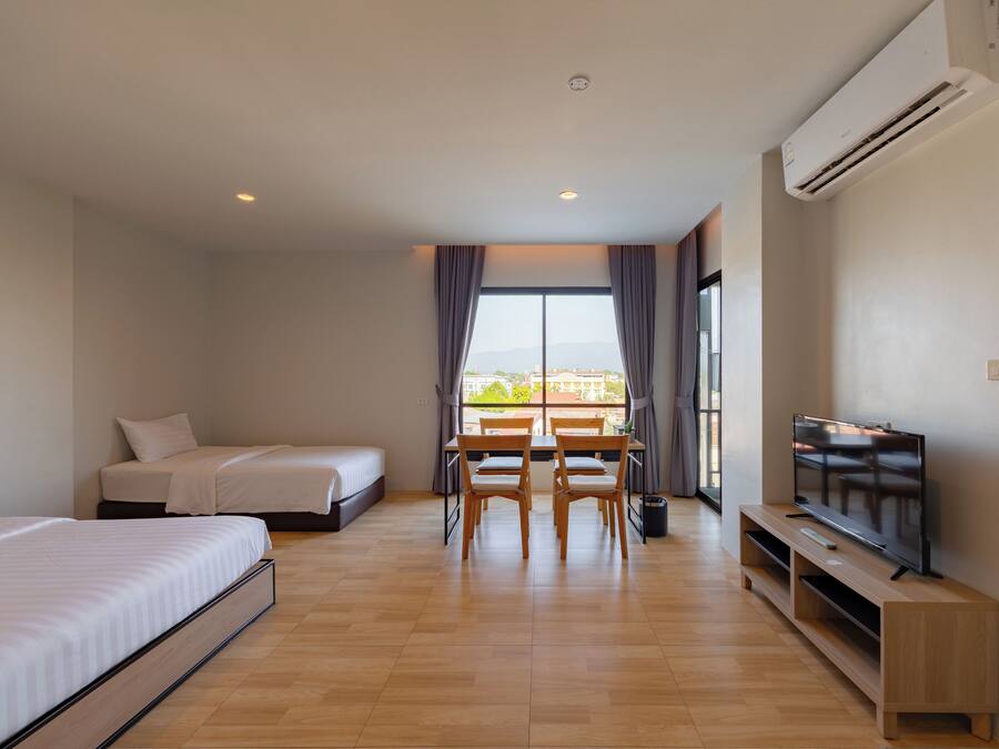 A hotel room with a bed, a TV, a dining table with chairs, and a large window.