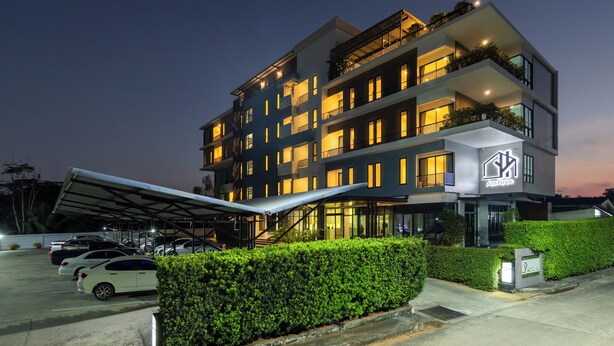 Un hotel de varios pisos con una zona de estacionamiento techada, un logotipo destacado y una fachada bien iluminada.