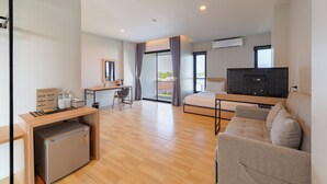 Habitación de hotel moderna con cama, escritorio, silla, refrigerador pequeño, televisión y balcón con cortinas.
