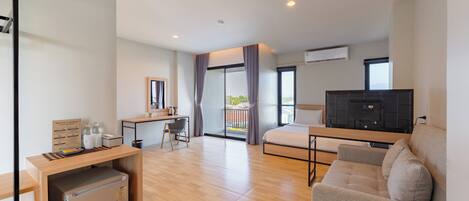 Habitación de hotel moderna con cama, escritorio, silla, refrigerador pequeño, televisión y balcón con cortinas.