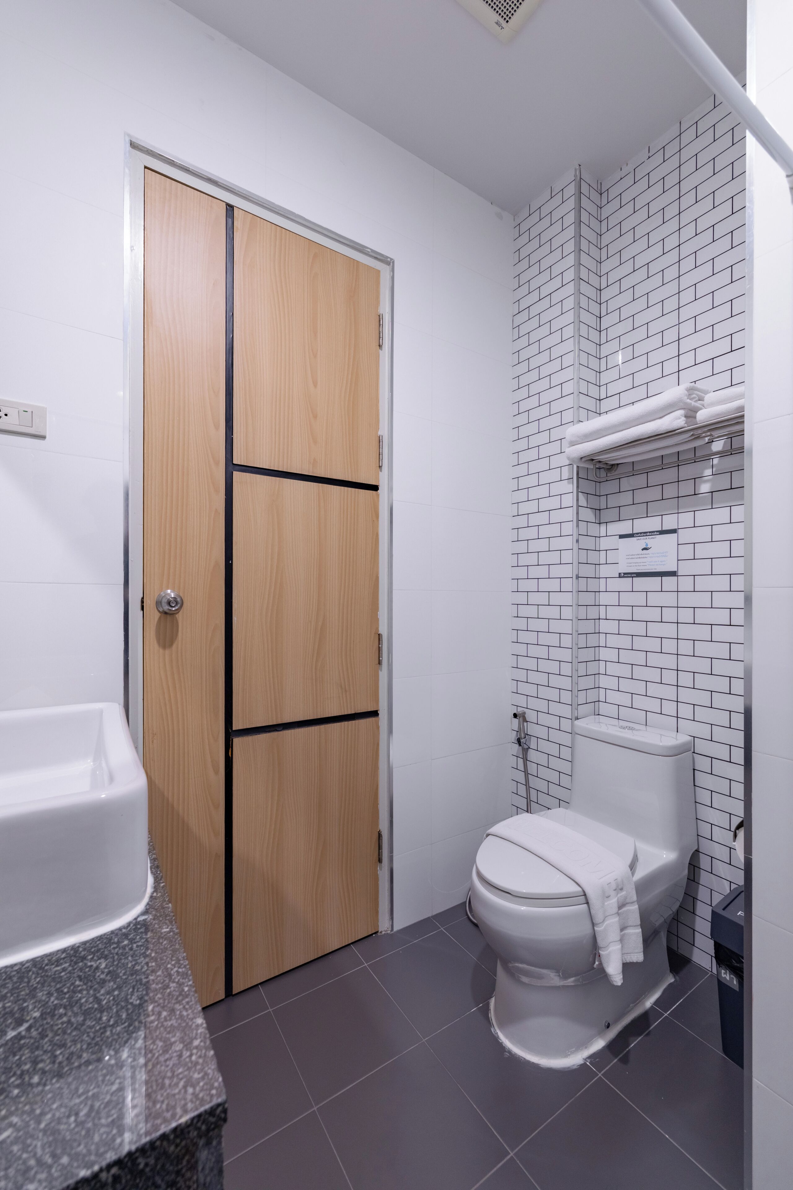 Ein Badezimmer mit Toilette, Waschbecken, einer Holztür und einer gefliesten Wand.