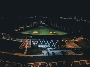 A stadium with a green field, a large illuminated logo, and a parking area.