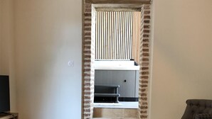 A living room with a wooden coffee table, a grey sofa, and a brick wall with a window. - CHEZ LULU, town house overlooking the Beuvron (Candé-sur-Beuvron)