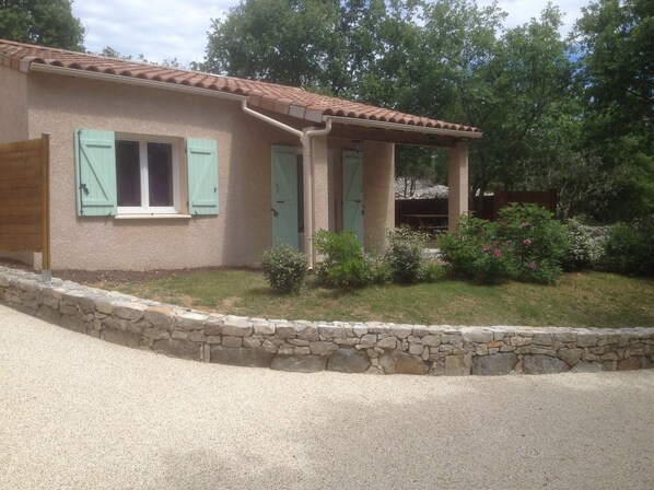 Une maison de plain-pied avec des fondations en pierre, un toit en tuiles et un petit jardin agrémenté d’arbustes et de fleurs.