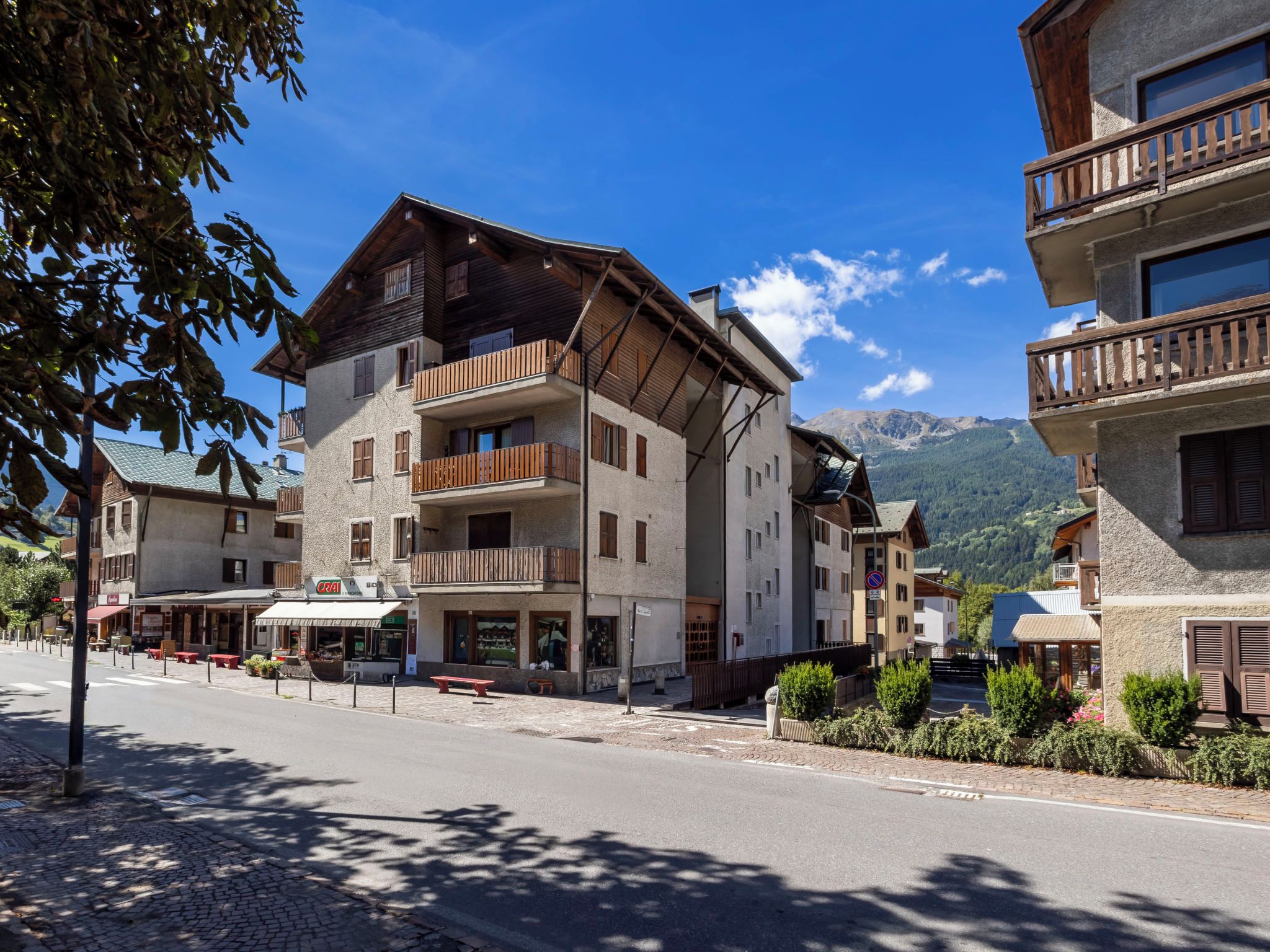 A multi-story building with balconies, a cobblestone street, and a mountain backdrop.