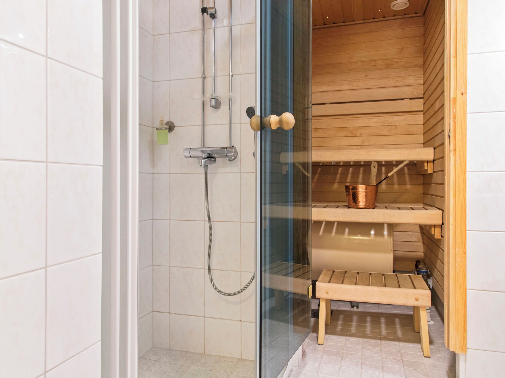 A shower with a glass door, a wooden shelf, and a small wooden stool.