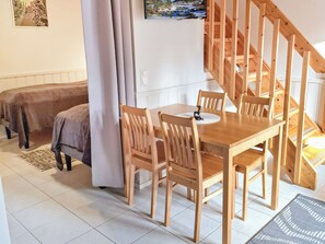 A room with a wooden dining table, chairs, a bed with a blanket, a staircase, and a wall-mounted picture.