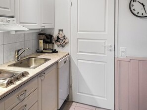 A kitchen with a double sink, stove, coffee maker, and a clock on the wall.