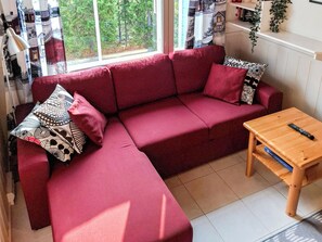 A red sofa with patterned cushions, a wooden coffee table, and a window with a view of trees.